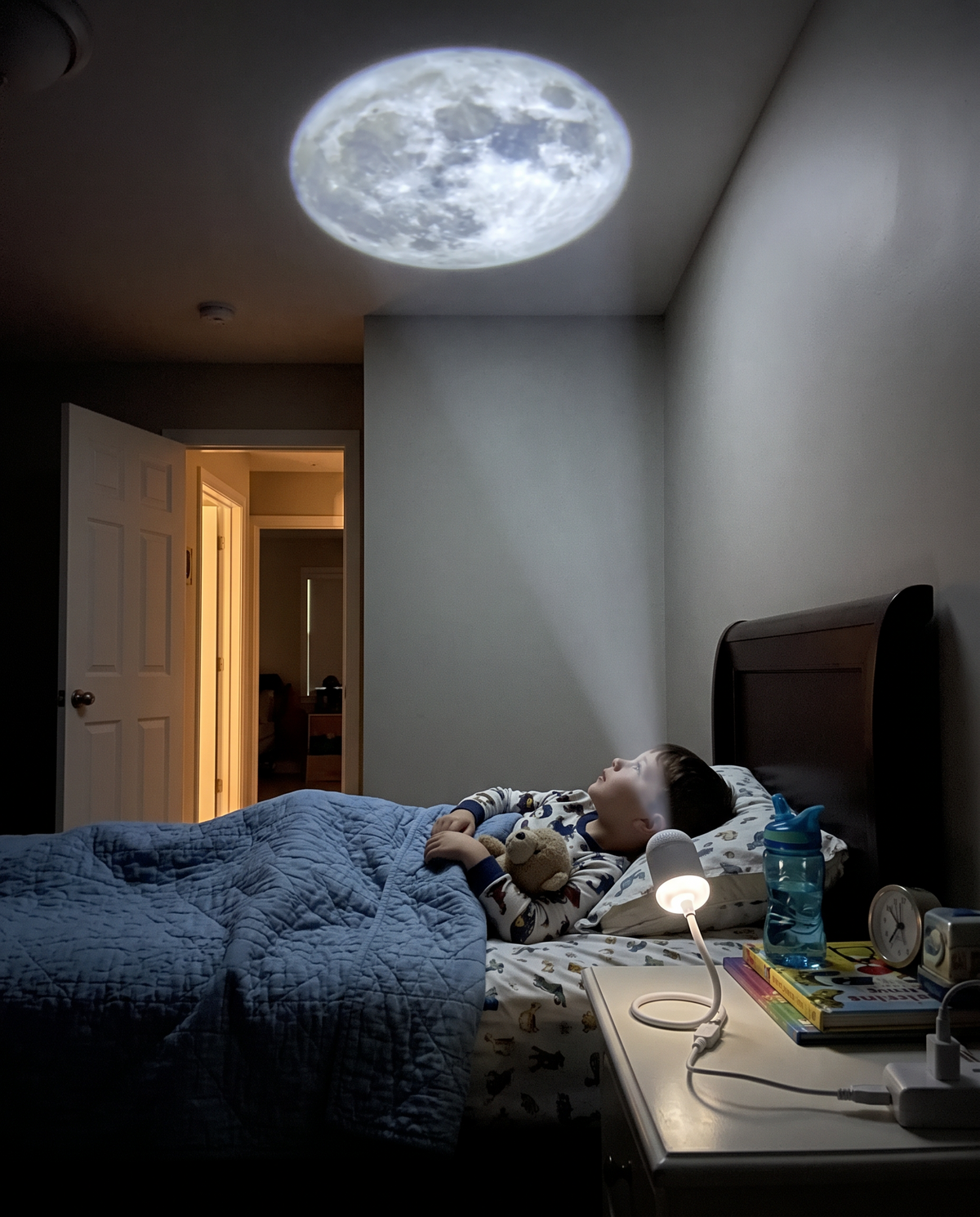 Boy in bed looking up at a projected moon and stars on his bedroom ceiling