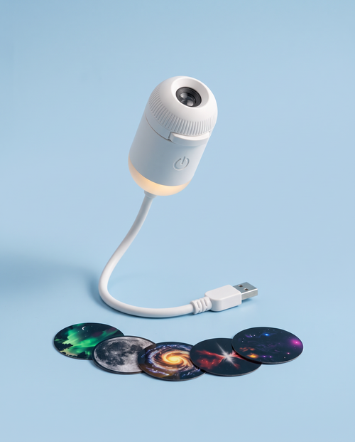 White mini galaxy projector with sky discs on a powder-blue background