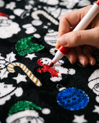 Close-up of a hand coloring a gingerbread man with a red fabric marker